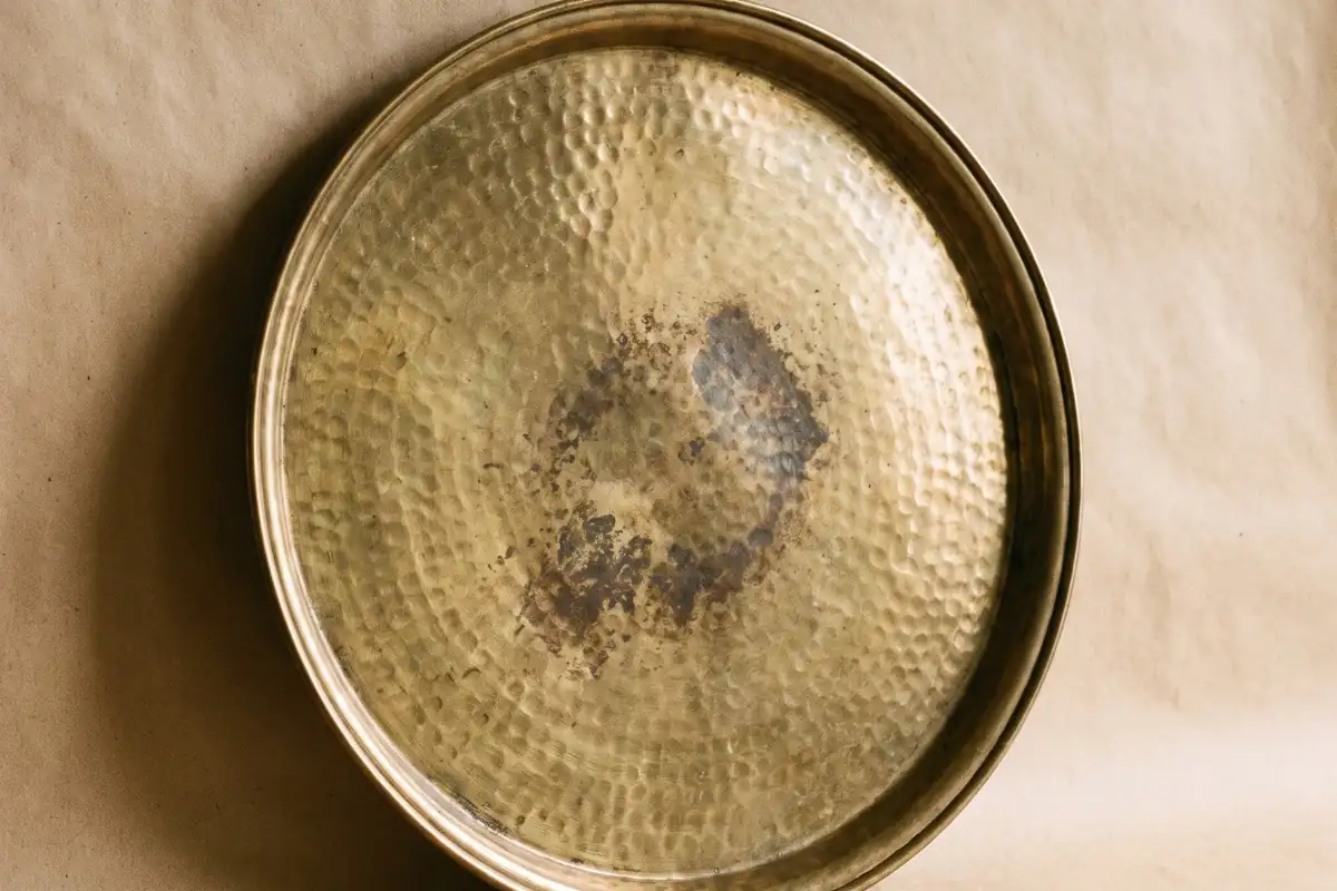 A close view of a small hammered brass dish with warm patina on a warm paper sweep — full width on the paper sweep.