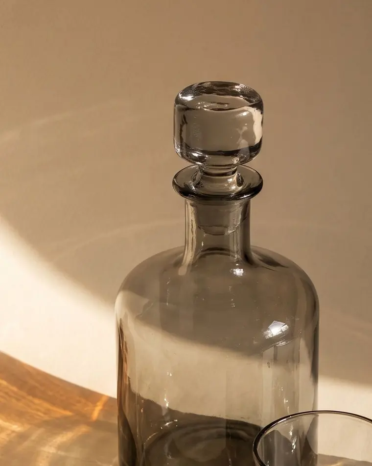 A close view of two heavy smoke grey hand-blown tumblers on a warm paper sweep.