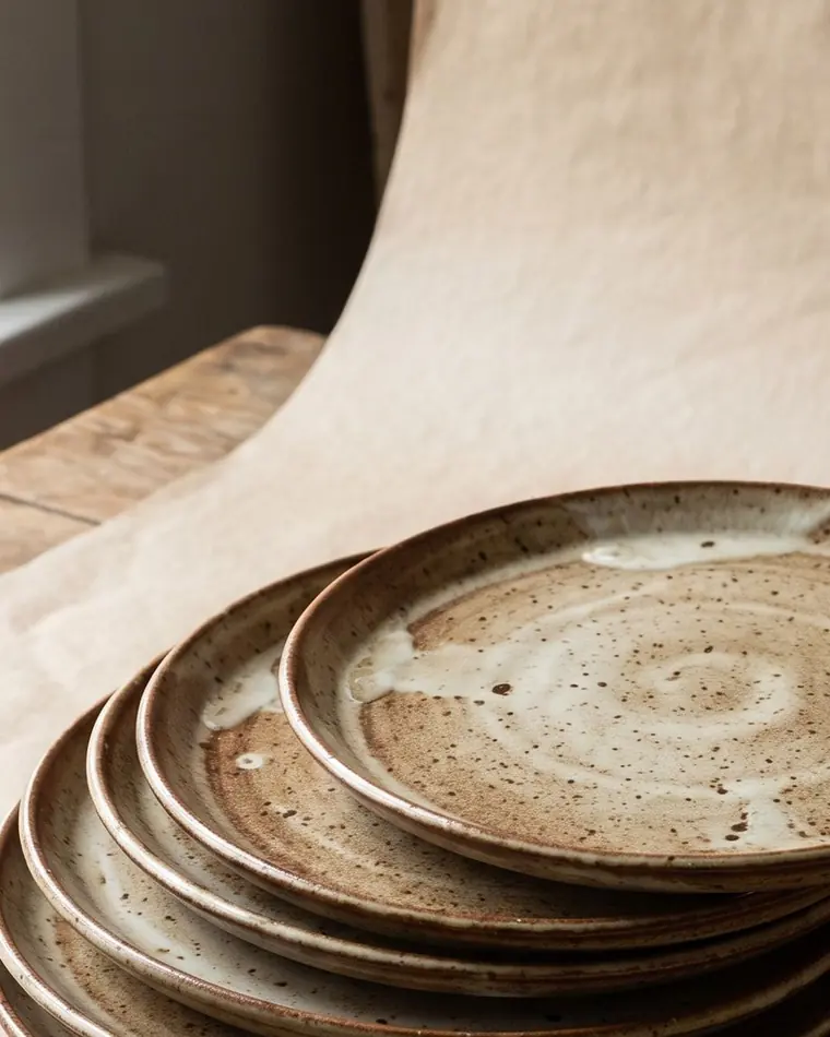 A close view of three shallow mottled iron-glazed stoneware serving bowls stacked on a warm paper sweep.