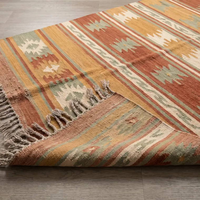 A close view of a handwoven wool flatweave runner in ochre with rust and sage banding — lower detail, showing the foot and the shadow.