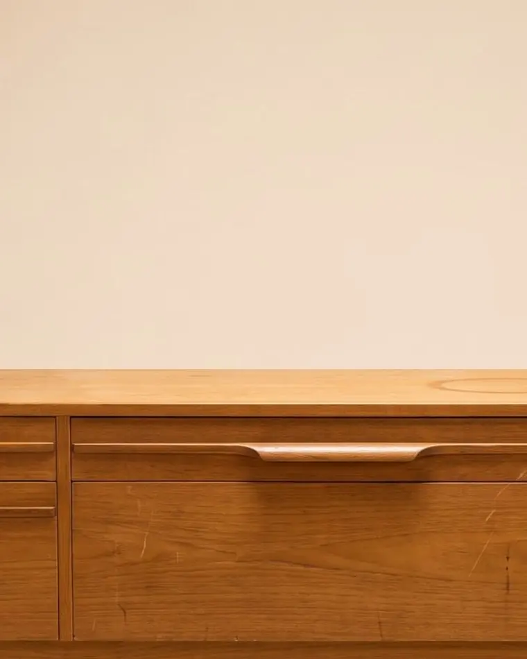 A close view of a Danish teak drawer bank with sculpted pulls against a warm paper backdrop.